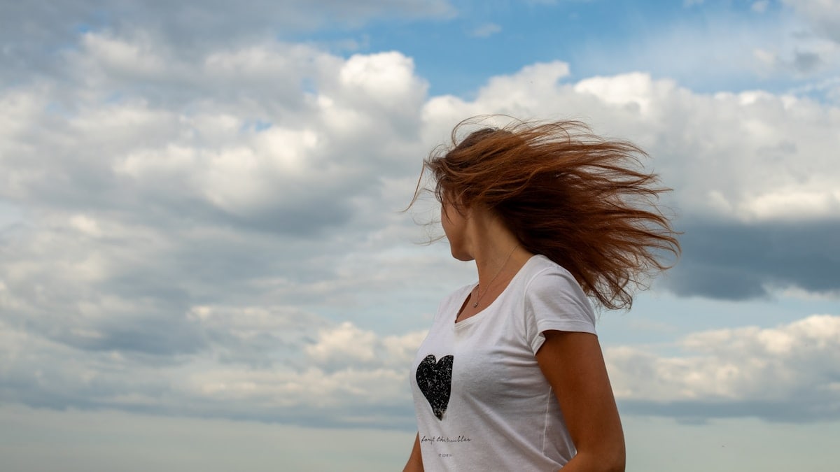 "A young woman with her hair blowing in the wind stands on the rocky shore of Kopli, Tallinn, looking out at the Baltic Sea under a dramatic cloudy sky."